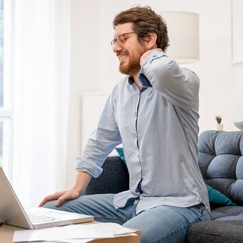 Mann mit Nackenschmerzen durch unergonomischen Arbeitsplatz im Homeoffice