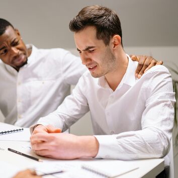 Mann gibt anderem Mann psychische Unterstützung indem er seine Hand auf dessen Schulter legt